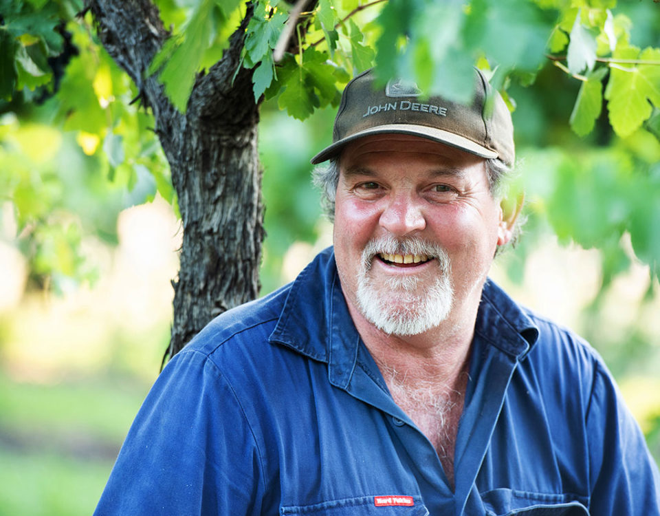 Grower Mark Lucas sitting amongst vines smiling with cap on